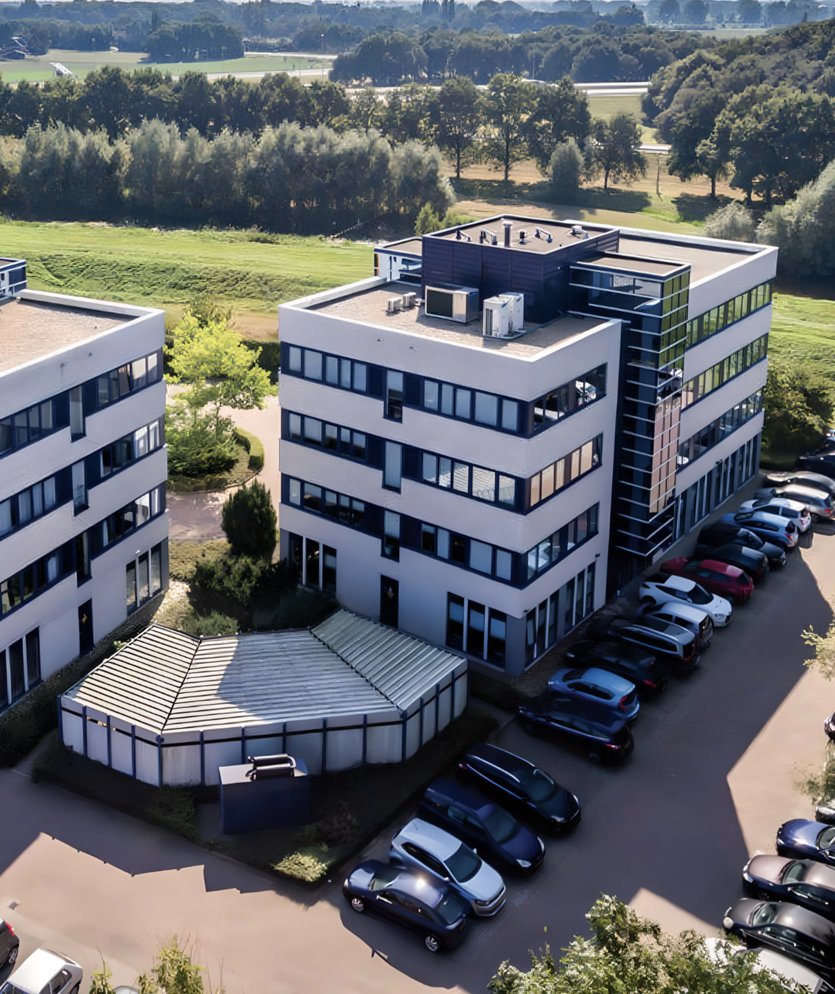 Aerial view of modern office buildings with a parking lot and green landscape in the background.