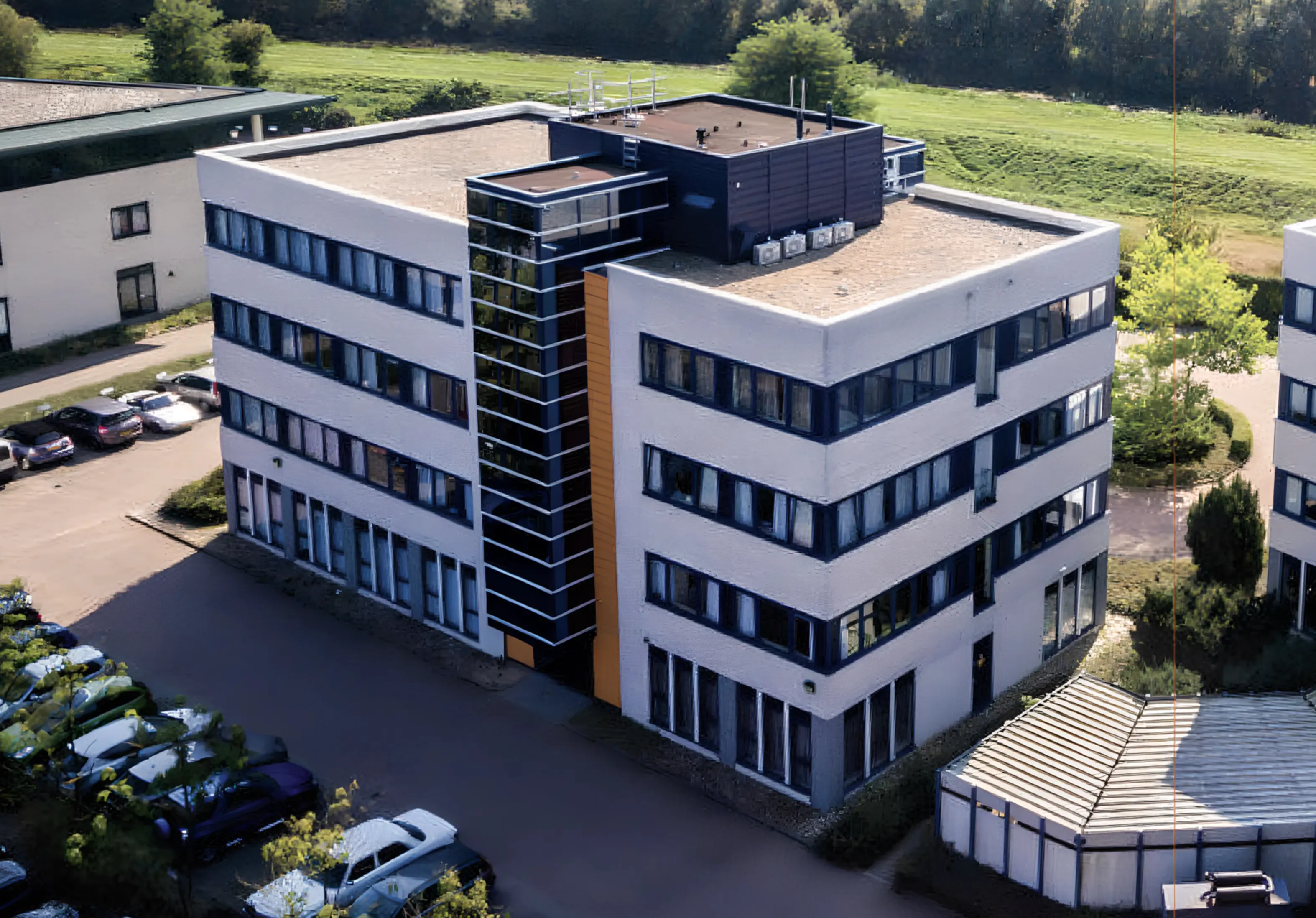 Aerial photo of a multi-story office building with large windows and nearby parking spaces.
